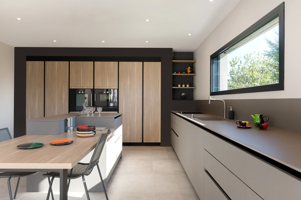 Inspiration for a contemporary eat-in kitchen in Lyon with grey cabinets, solid surface benchtops, grey splashback, black appliances, ceramic floors, with island, grey floor, grey benchtop, a double-bowl sink and flat-panel cabinets.