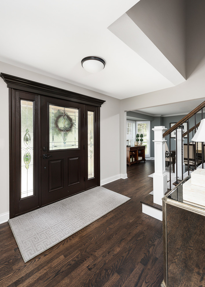 Design ideas for a large transitional foyer in Chicago with grey walls, dark hardwood floors, a pivot front door, a dark wood front door and brown floor.