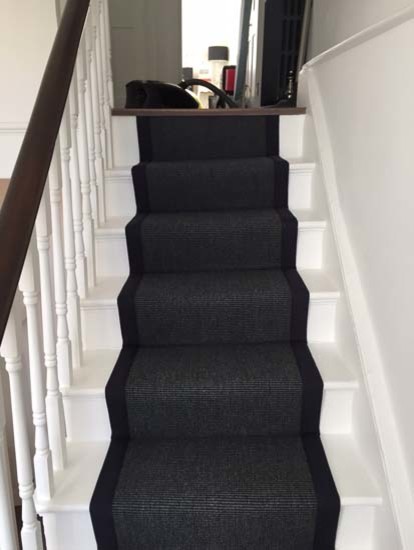 This is an example of a transitional carpeted u-shaped staircase in London with carpet risers and wood railing.