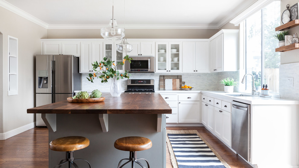 This is an example of a mid-sized country l-shaped separate kitchen in Sacramento with an undermount sink, shaker cabinets, grey splashback, stone tile splashback, stainless steel appliances, medium hardwood floors, with island, white cabinets and marble benchtops.