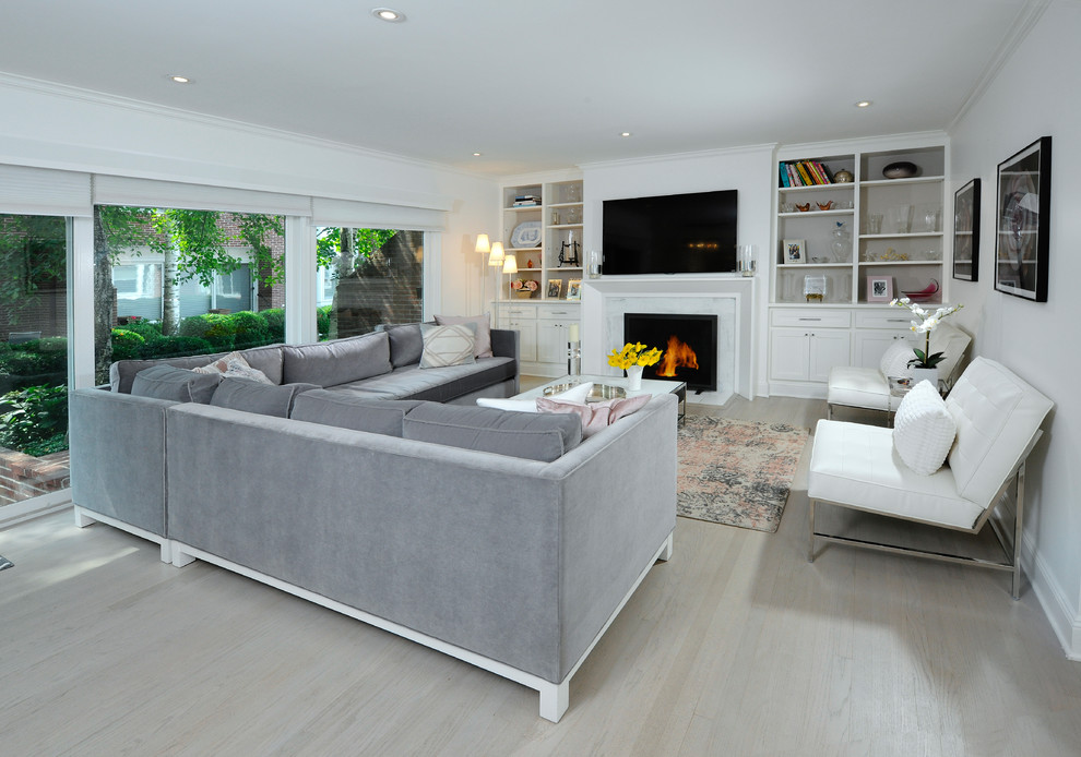 Photo of a small transitional living room in New York with white walls, light hardwood floors, a standard fireplace, a wall-mounted tv and beige floor.
