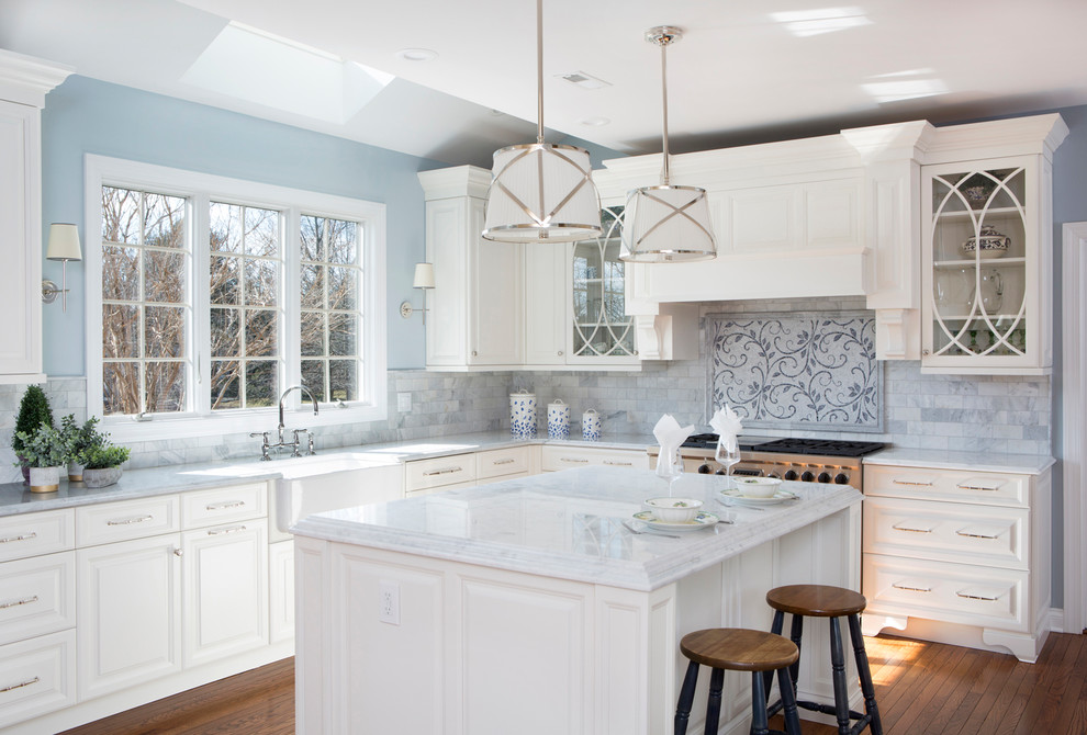 Photo of a mid-sized traditional l-shaped kitchen in Philadelphia with a farmhouse sink, glass-front cabinets, white cabinets, multi-coloured splashback, stainless steel appliances, medium hardwood floors, with island and white benchtop.