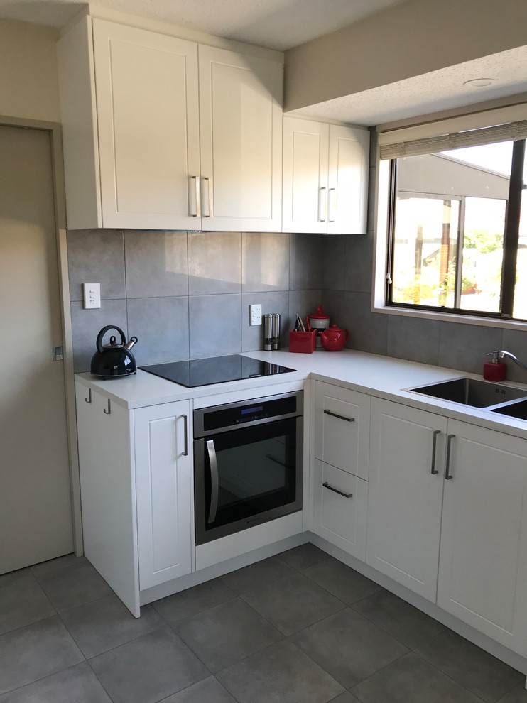 Mid-sized contemporary galley open plan kitchen in Christchurch with a double-bowl sink, flat-panel cabinets, white cabinets, laminate benchtops, grey splashback, porcelain splashback, stainless steel appliances, porcelain floors, grey floor and white benchtop.