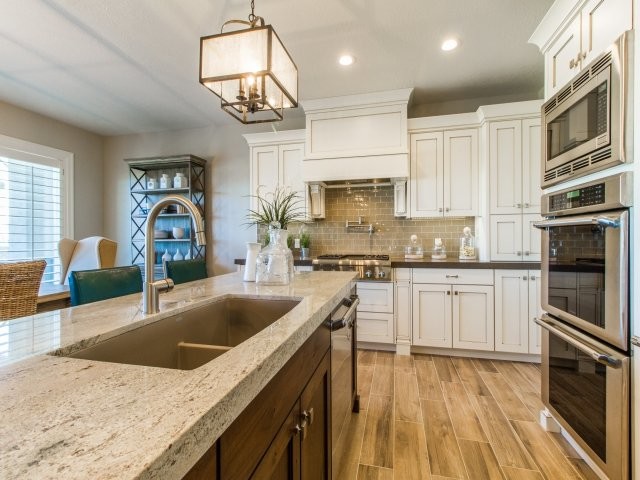 This is an example of a mid-sized arts and crafts l-shaped eat-in kitchen in Salt Lake City with a double-bowl sink, shaker cabinets, white cabinets, granite benchtops, green splashback, subway tile splashback, stainless steel appliances, porcelain floors, with island and brown floor.