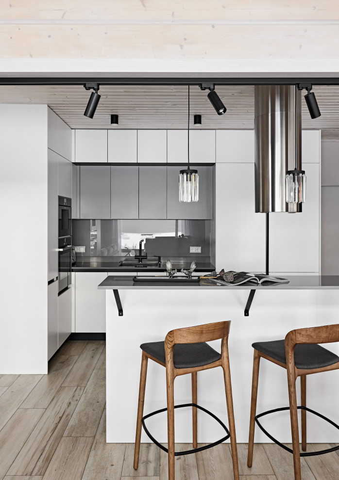 Mid-sized contemporary l-shaped eat-in kitchen in Saint Petersburg with an undermount sink, flat-panel cabinets, white cabinets, solid surface benchtops, grey splashback, engineered quartz splashback, black appliances, medium hardwood floors, with island, beige floor, grey benchtop and wood.