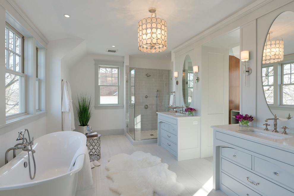Beach style master bathroom in Minneapolis with beaded inset cabinets, grey cabinets, a freestanding tub, a corner shower, gray tile, ceramic tile, white walls, porcelain floors, an undermount sink, solid surface benchtops and a hinged shower door.