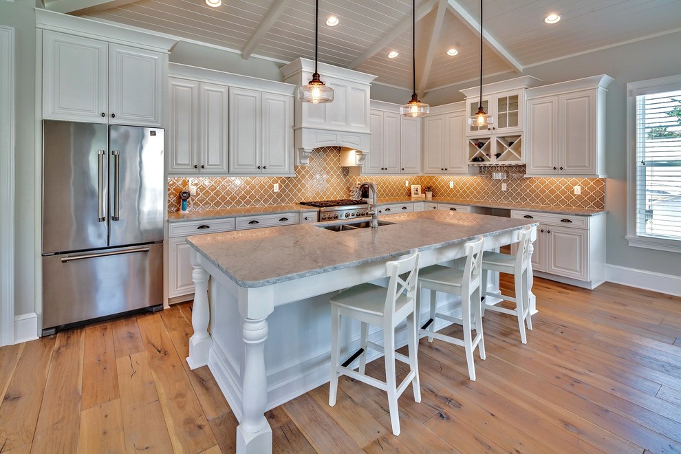 Large beach style l-shaped open plan kitchen in Jacksonville with a double-bowl sink, raised-panel cabinets, white cabinets, marble benchtops, brown splashback, ceramic splashback, stainless steel appliances, medium hardwood floors and with island.