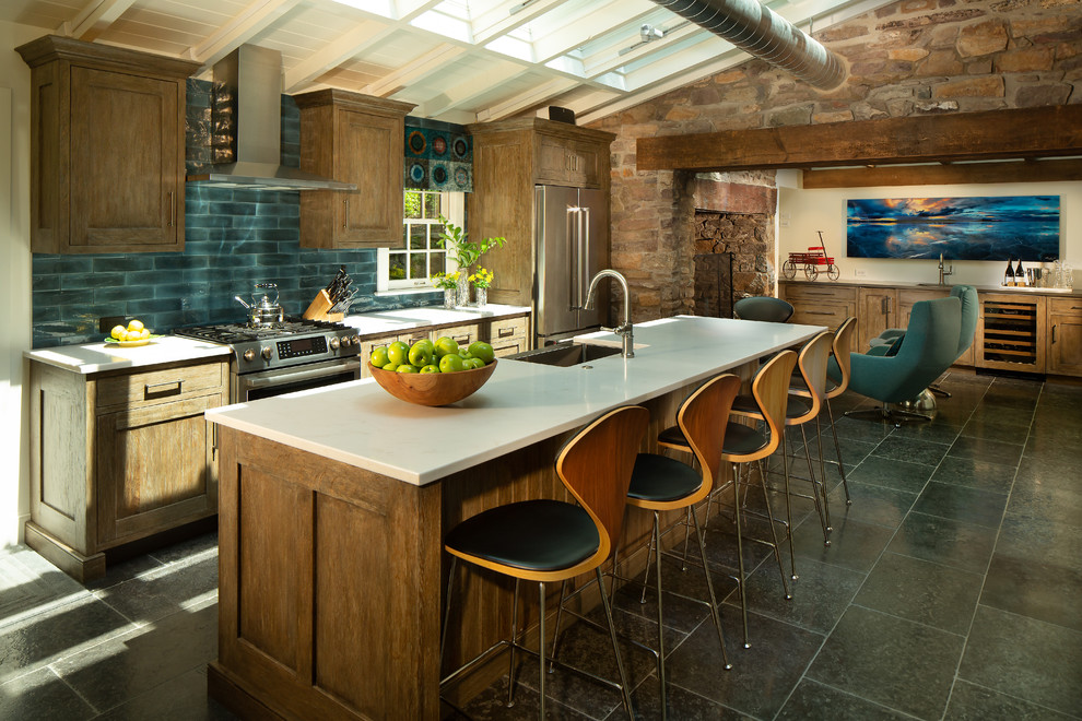 Country eat-in kitchen in Philadelphia with a farmhouse sink, shaker cabinets, dark wood cabinets, blue splashback, subway tile splashback, stainless steel appliances, with island, black floor and white benchtop.