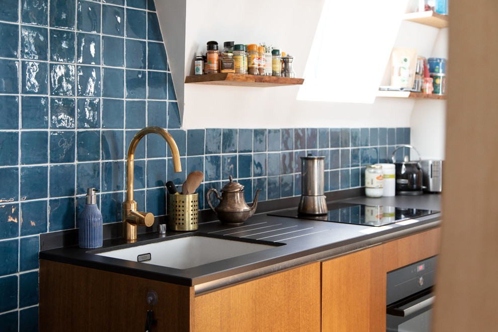 Design ideas for a small mediterranean galley open plan kitchen in Other with flat-panel cabinets, light wood cabinets, blue splashback, ceramic splashback, black appliances, ceramic floors, blue floor, black benchtop, an undermount sink, solid surface benchtops and a peninsula.