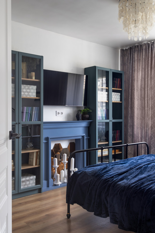 На фото: хозяйская спальня среднего размера в современном стиле с белыми стенами, полом из винила, стандартным камином, фасадом камина из дерева, коричневым полом и синими шторами