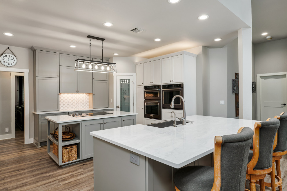 Inspiration for a mid-sized transitional u-shaped vinyl floor and brown floor kitchen pantry remodel in Austin with a farmhouse sink, shaker cabinets, white cabinets, quartz countertops, white backsplash, marble backsplash, black appliances, two islands and white countertops