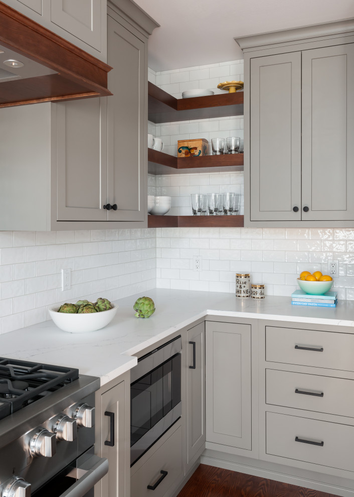 Inspiration for a mid-sized transitional l-shaped kitchen in Seattle with an undermount sink, shaker cabinets, grey cabinets, quartz benchtops, white splashback, subway tile splashback, stainless steel appliances, medium hardwood floors, with island, brown floor and white benchtop.