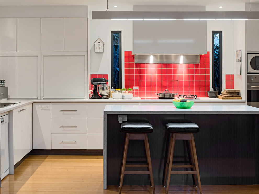 Large modern l-shaped eat-in kitchen in Brisbane with a double-bowl sink, flat-panel cabinets, white cabinets, quartz benchtops, red splashback, ceramic splashback, stainless steel appliances, light hardwood floors, with island, beige floor and white benchtop.