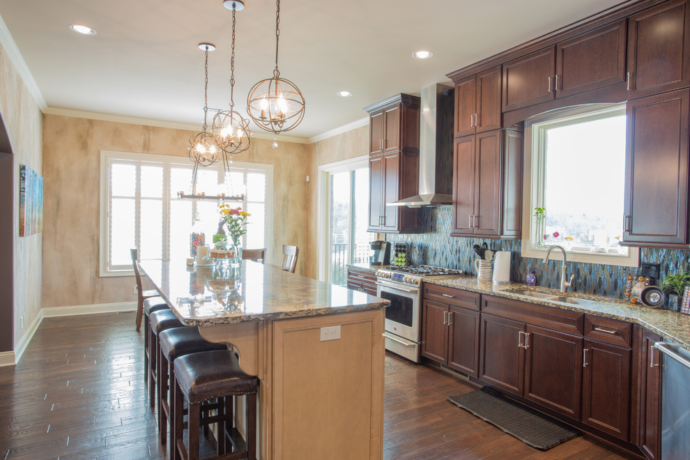 Inspiration for a large transitional galley medium tone wood floor and brown floor enclosed kitchen remodel with an undermount sink, raised-panel cabinets, dark wood cabinets, granite countertops, multicolored backsplash, mosaic tile backsplash, stainless steel appliances and an island