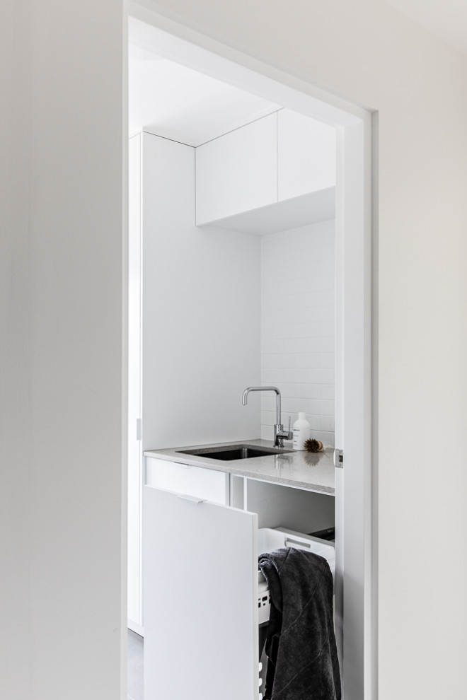 Design ideas for a small contemporary single-wall dedicated laundry room in Sydney with an undermount sink, white cabinets, quartz benchtops, white walls, ceramic floors, a concealed washer and dryer, grey floor and grey benchtop.