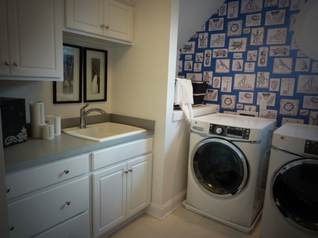 Photo of a modern laundry room in Richmond with an utility sink, raised-panel cabinets, white cabinets, laminate benchtops, white walls, vinyl floors and a side-by-side washer and dryer.