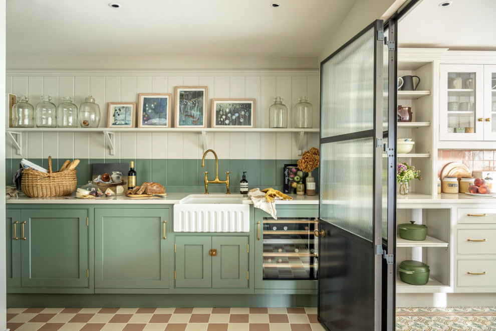 Photo of a traditional eat-in kitchen in Buckinghamshire with a farmhouse sink, shaker cabinets, green cabinets, solid surface benchtops, pink splashback, ceramic splashback, black appliances, ceramic floors, with island and white benchtop.