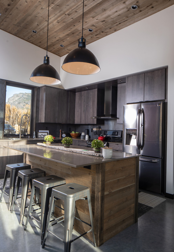Small industrial l-shaped open plan kitchen in Seattle with an undermount sink, flat-panel cabinets, black cabinets, solid surface benchtops, brown splashback, stainless steel appliances, concrete floors, with island, grey floor and brown benchtop.