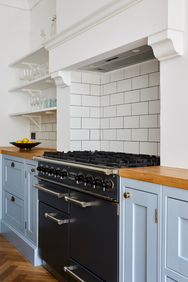 Large traditional l-shaped open plan kitchen in London with a drop-in sink, shaker cabinets, grey cabinets, wood benchtops, white splashback, subway tile splashback, stainless steel appliances, medium hardwood floors, with island, brown floor and multi-coloured benchtop.