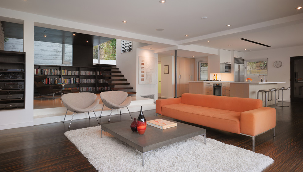 This is an example of a small modern open concept living room in Los Angeles with a library, white walls, dark hardwood floors and brown floor.