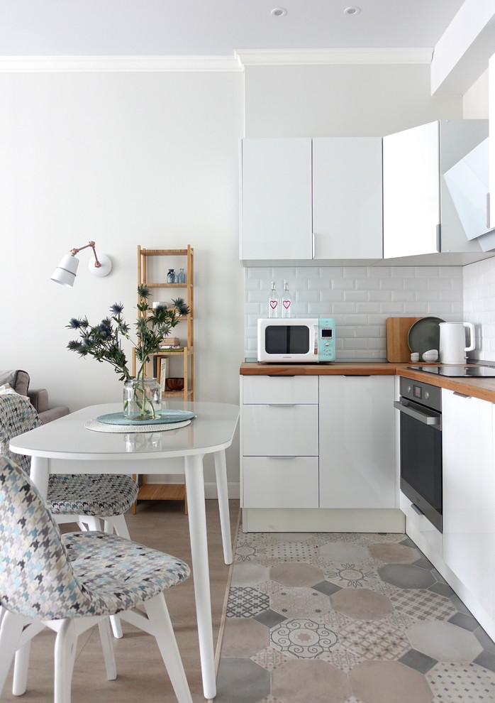 This is an example of a contemporary l-shaped kitchen in Moscow with flat-panel cabinets, white cabinets, wood benchtops, white splashback, subway tile splashback, stainless steel appliances, multi-coloured floor and brown benchtop.