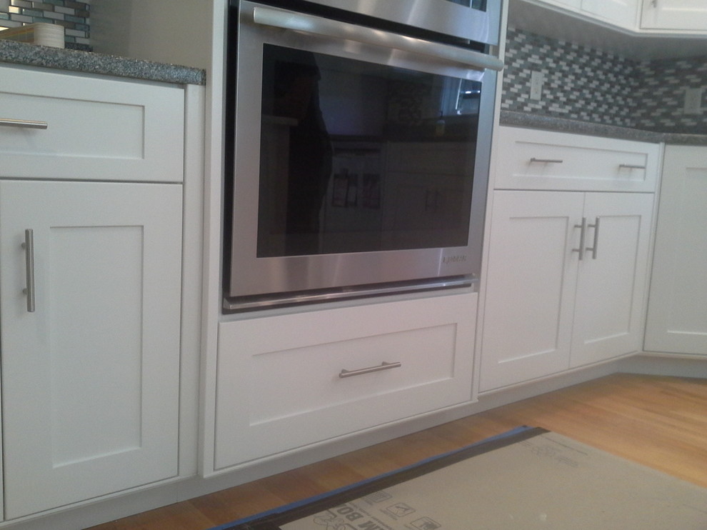 Large transitional light wood floor eat-in kitchen photo in Boston with recessed-panel cabinets, white cabinets, granite countertops, multicolored backsplash, glass tile backsplash and stainless steel appliances
