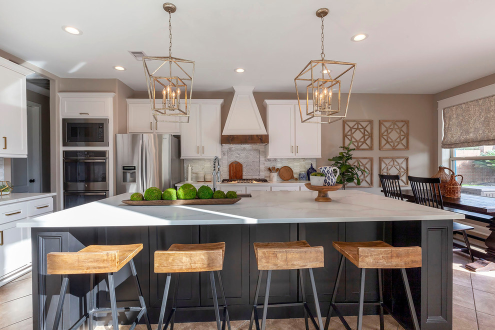 This is an example of a transitional eat-in kitchen in Houston with a farmhouse sink, shaker cabinets, white cabinets, quartz benchtops, beige splashback, marble splashback, stainless steel appliances, ceramic floors, with island, beige floor and white benchtop.