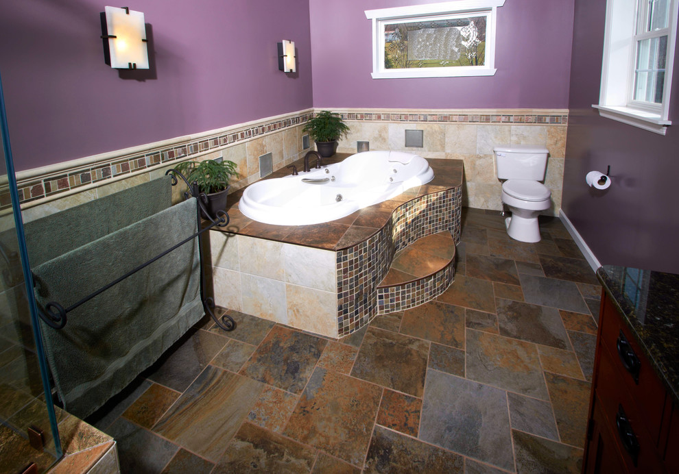 This is an example of a large mediterranean master bathroom in Other with an undermount sink, granite benchtops, a drop-in tub, a two-piece toilet, brown tile, porcelain tile, purple walls, raised-panel cabinets, brown cabinets, a corner shower and slate floors.