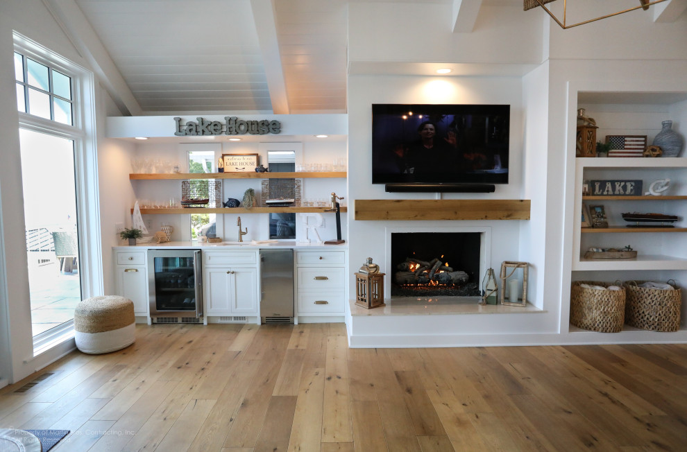 Exempel på ett stort maritimt allrum med öppen planlösning, med en hemmabar, vita väggar, mellanmörkt trägolv, en standard öppen spis och en väggmonterad TV