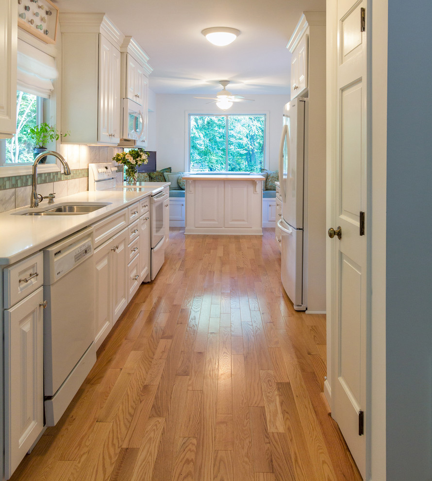 Inspiration for a transitional galley enclosed kitchen remodel in Raleigh with an undermount sink, raised-panel cabinets, white cabinets, quartz countertops, gray backsplash, porcelain backsplash and white appliances