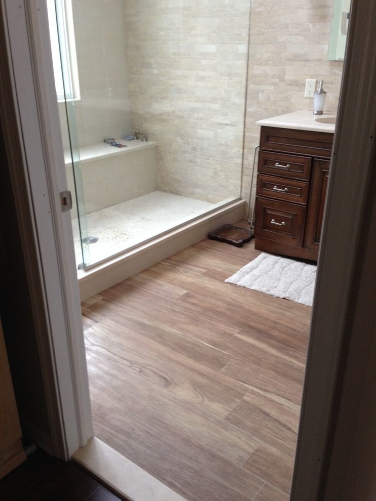 Inspiration for a large traditional master bathroom in New York with raised-panel cabinets, dark wood cabinets, an alcove shower, beige tile, stone tile, beige walls, medium hardwood floors, an undermount sink, engineered quartz benchtops, brown floor and a hinged shower door.