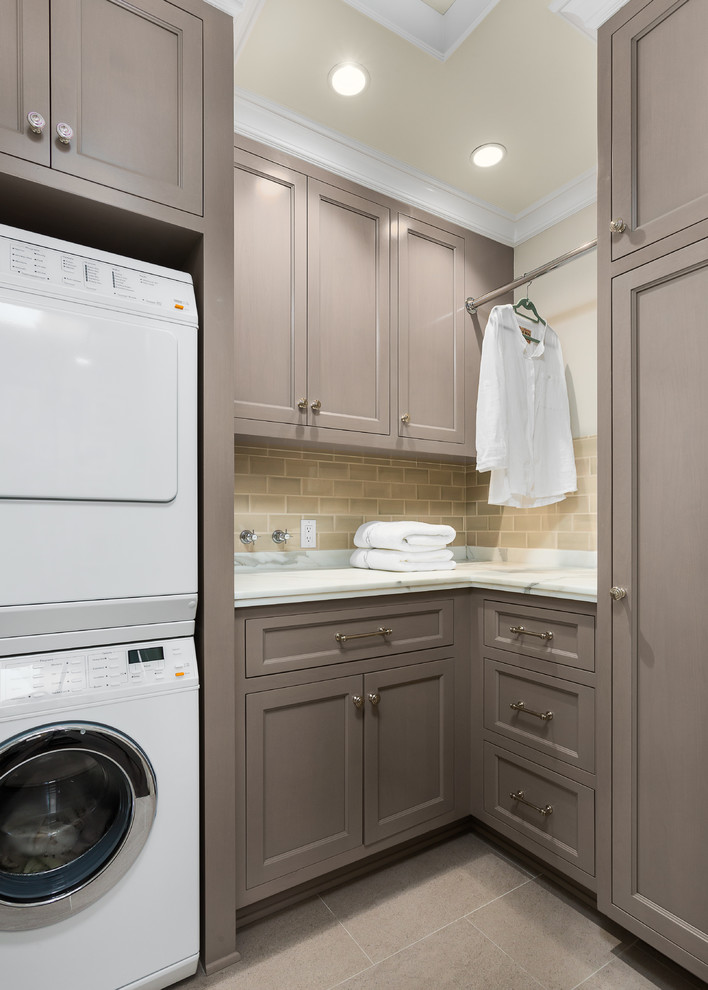 Mid-sized traditional l-shaped dedicated laundry room in Los Angeles with recessed-panel cabinets, grey cabinets, marble benchtops, beige walls, a stacked washer and dryer, grey floor and porcelain floors.