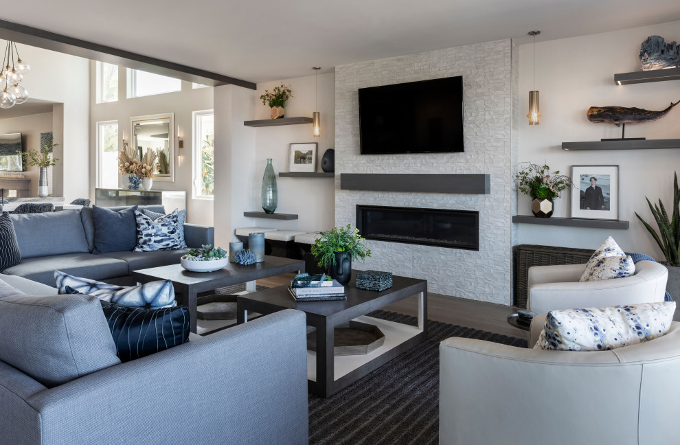 Expansive modern open plan living room in Orange County with white walls, light hardwood flooring, a standard fireplace, a tiled fireplace surround, a wall mounted tv and grey floors.