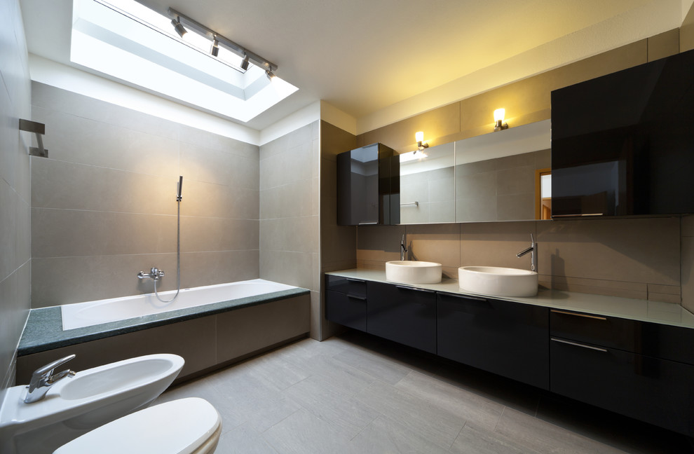 Inspiration for a large modern master bathroom in Toronto with flat-panel cabinets, black cabinets, an undermount tub, a shower/bathtub combo, a wall-mount toilet, beige tile, stone tile, beige walls, light hardwood floors, a vessel sink, glass benchtops, brown floor and an open shower.