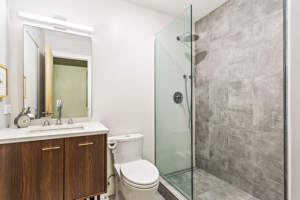 Photo of a mid-sized contemporary master bathroom in Chicago with flat-panel cabinets, medium wood cabinets, a shower/bathtub combo, a one-piece toilet, multi-coloured tile, marble, beige walls, an undermount sink, engineered quartz benchtops, a hinged shower door and white benchtops.