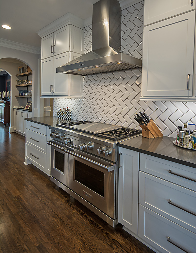 This is an example of a large transitional l-shaped open plan kitchen in Atlanta with a farmhouse sink, shaker cabinets, white cabinets, quartzite benchtops, white splashback, subway tile splashback, stainless steel appliances, medium hardwood floors, with island and brown floor.