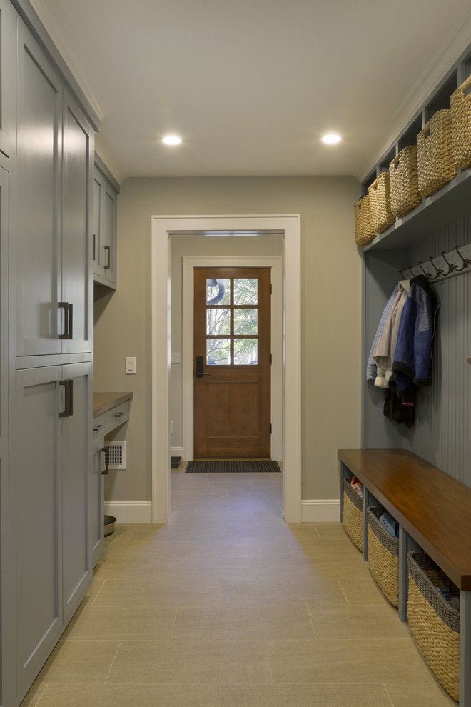 Photo of a large transitional mudroom in New York with grey walls, porcelain floors, a single front door, a medium wood front door and beige floor.