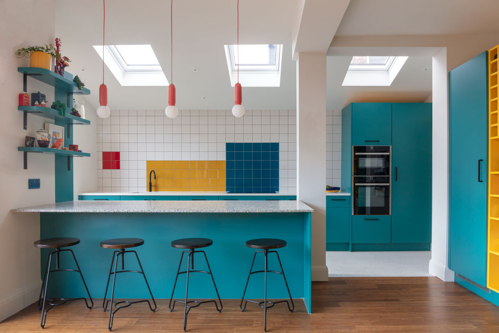 Contemporary kitchen in Manchester with flat-panel cabinets, turquoise cabinets, multi-coloured splashback, black appliances and a breakfast bar.