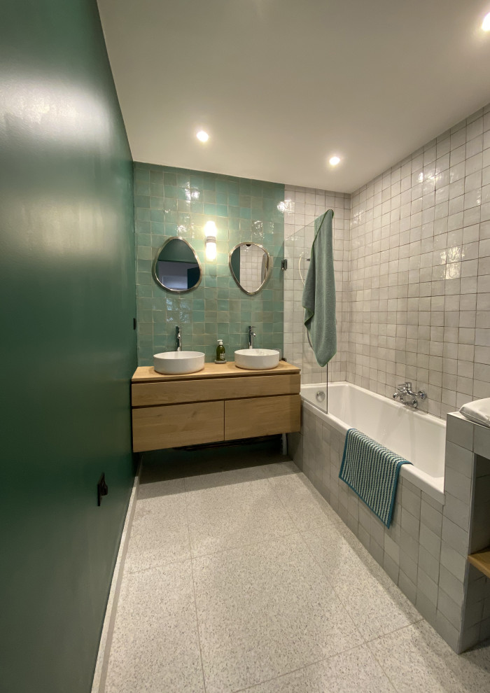 パリにある中くらいな北欧スタイルのおしゃれな子供用バスルーム (淡色木目調キャビネット、アンダーマウント型浴槽、シャワー付き浴槽	、緑のタイル、テラコッタタイル、緑の壁、テラゾーの床、オーバーカウンターシンク、ラミネートカウンター、グレーの床、開き戸のシャワー、ブラウンの洗面カウンター、洗面台2つ、フローティング洗面台) の写真