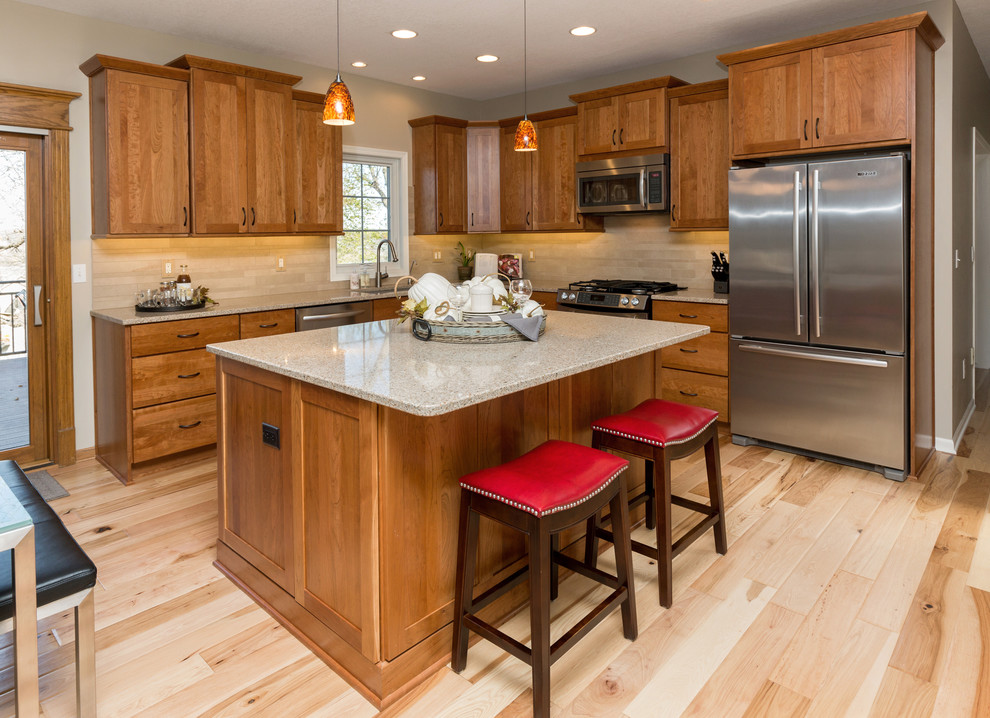 Example of a mid-sized transitional l-shaped light wood floor open concept kitchen design with an undermount sink, recessed-panel cabinets, medium tone wood cabinets, quartz countertops, beige backsplash, stone tile backsplash, stainless steel appliances and an island