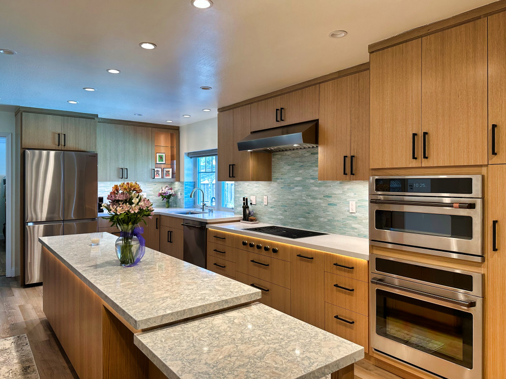 This is an example of a large asian l-shaped eat-in kitchen in San Francisco with an undermount sink, flat-panel cabinets, medium wood cabinets, quartzite benchtops, metallic splashback, glass tile splashback, stainless steel appliances, medium hardwood floors, with island, brown floor and white benchtop.