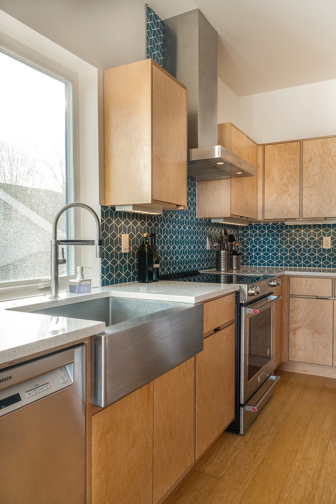 This is an example of a mid-sized modern l-shaped open plan kitchen in Seattle with a farmhouse sink, flat-panel cabinets, light wood cabinets, quartz benchtops, blue splashback, cement tile splashback, stainless steel appliances, bamboo floors, with island, brown floor and white benchtop.