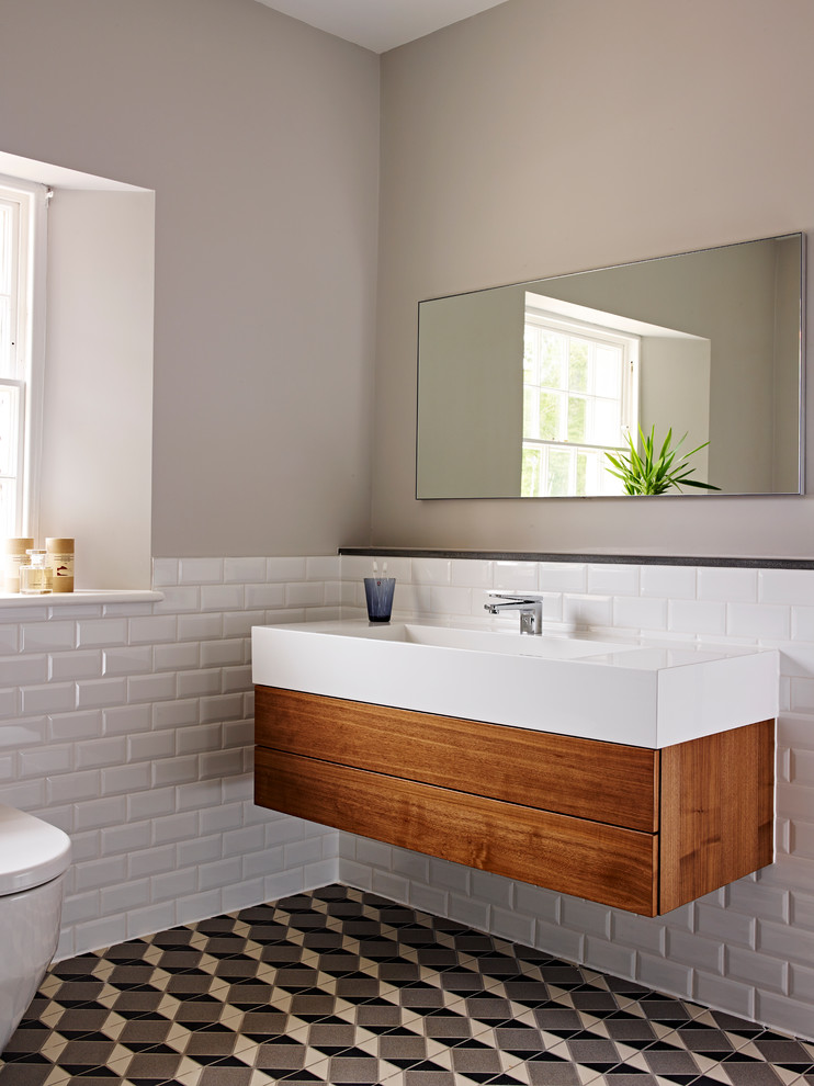 Design ideas for a mid-sized traditional bathroom in Devon with a wall-mount sink, flat-panel cabinets, medium wood cabinets, a one-piece toilet, white tile and ceramic floors.