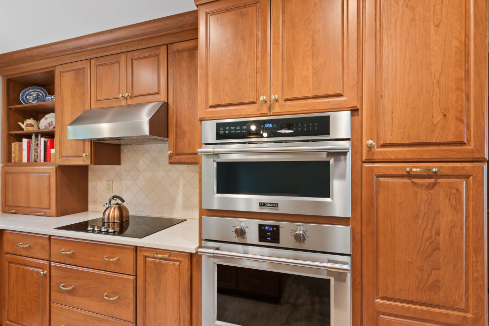 Inspiration for a mid-sized traditional l-shaped eat-in kitchen in Milwaukee with an undermount sink, raised-panel cabinets, brown cabinets, quartz benchtops, beige splashback, stone tile splashback, stainless steel appliances, vinyl floors, with island, brown floor and beige benchtop.