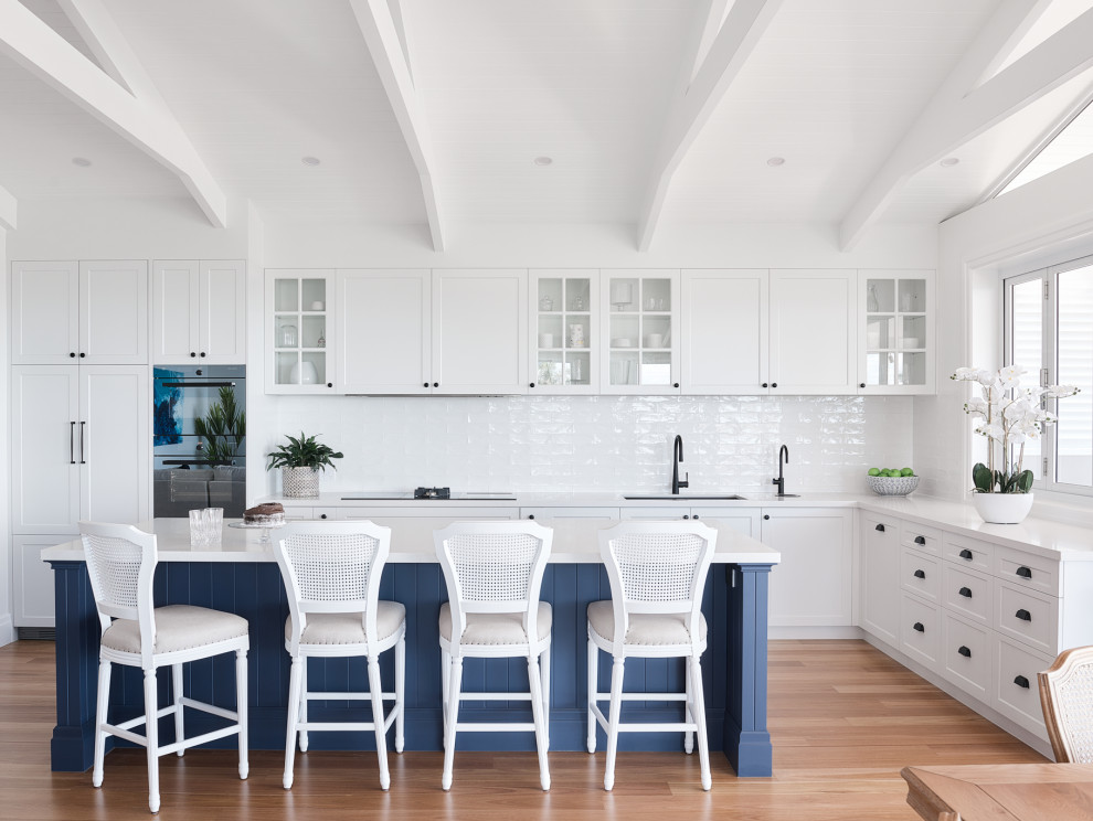 Design ideas for a large beach style l-shaped eat-in kitchen in Brisbane with an undermount sink, shaker cabinets, white cabinets, white splashback, panelled appliances, with island, beige floor and white benchtop.