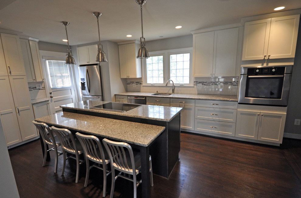 Example of a mid-sized transitional l-shaped dark wood floor and brown floor open concept kitchen design in DC Metro with an undermount sink, shaker cabinets, white cabinets, white backsplash, subway tile backsplash, stainless steel appliances and an island