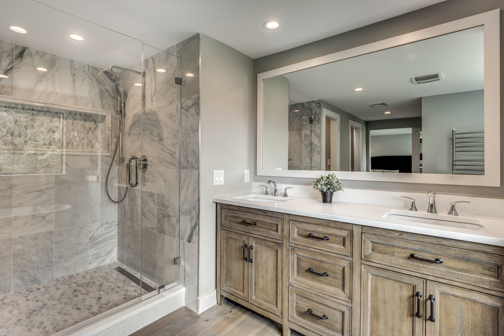 Photo of a mid-sized contemporary master bathroom in Boston with recessed-panel cabinets, medium wood cabinets, a freestanding tub, an alcove shower, grey walls, medium hardwood floors, an undermount sink, solid surface benchtops, brown floor and a hinged shower door.