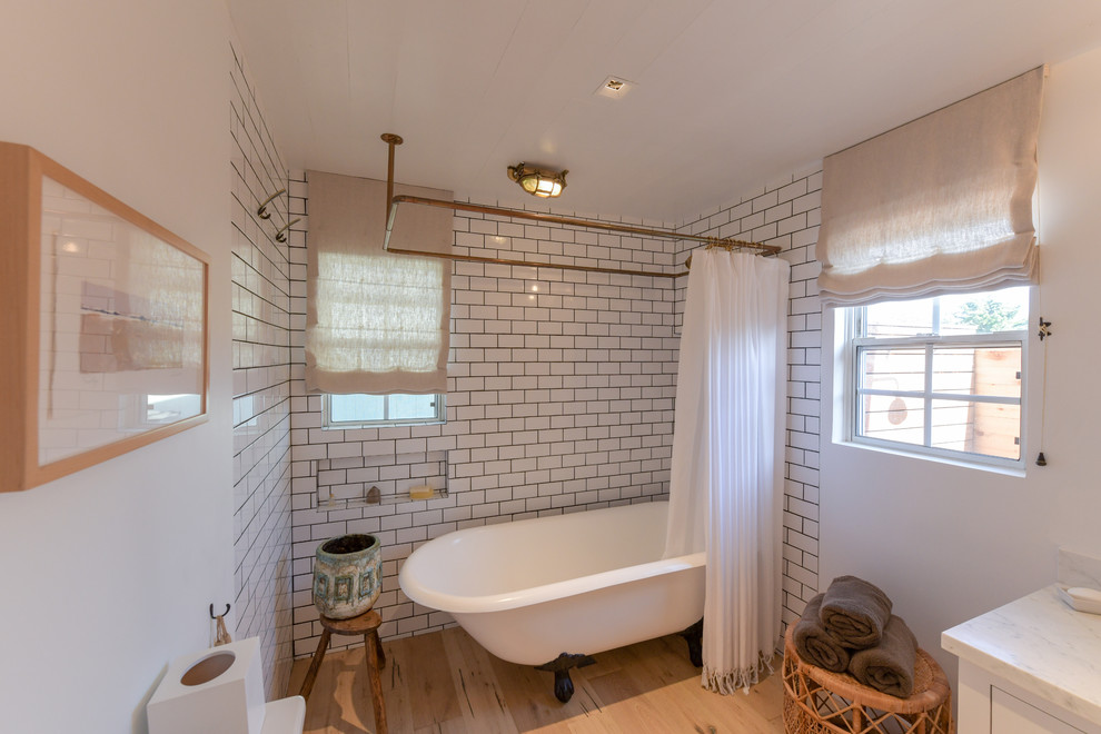 Mid-sized transitional bathroom in Los Angeles with shaker cabinets, white cabinets, a claw-foot tub, a shower/bathtub combo, white tile, subway tile, white walls, light hardwood floors, an undermount sink, marble benchtops, beige floor, a shower curtain and white benchtops.
