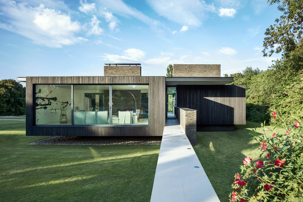 Photo of a mid-sized contemporary two-storey black house exterior in Hampshire with wood siding and a flat roof.