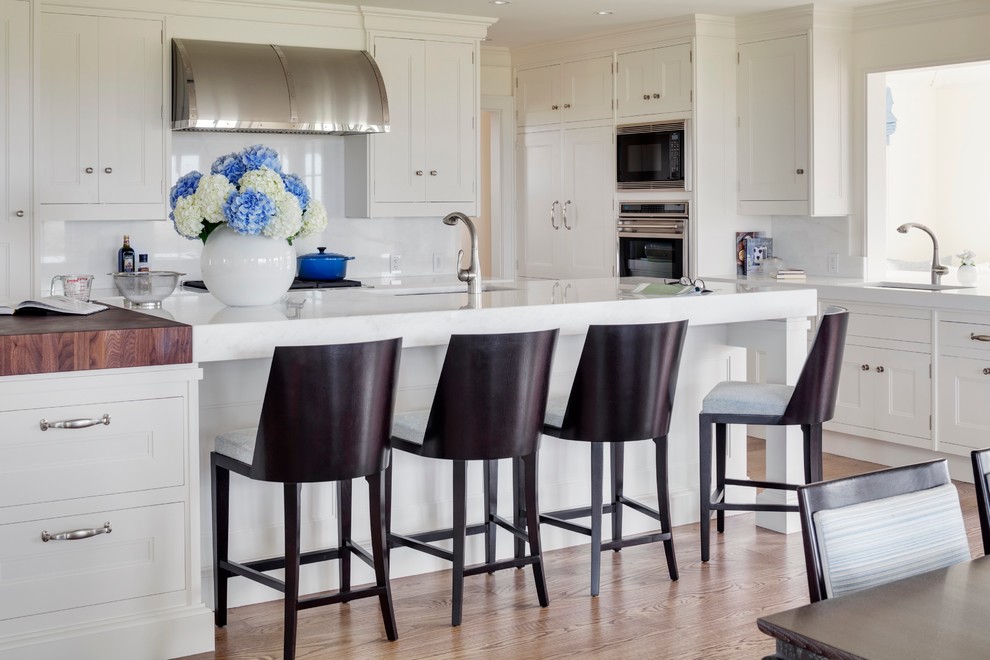 Inspiration for a large contemporary l-shaped eat-in kitchen in Boston with an undermount sink, recessed-panel cabinets, white cabinets, marble benchtops, white splashback, stone slab splashback, stainless steel appliances, medium hardwood floors, with island and brown floor.